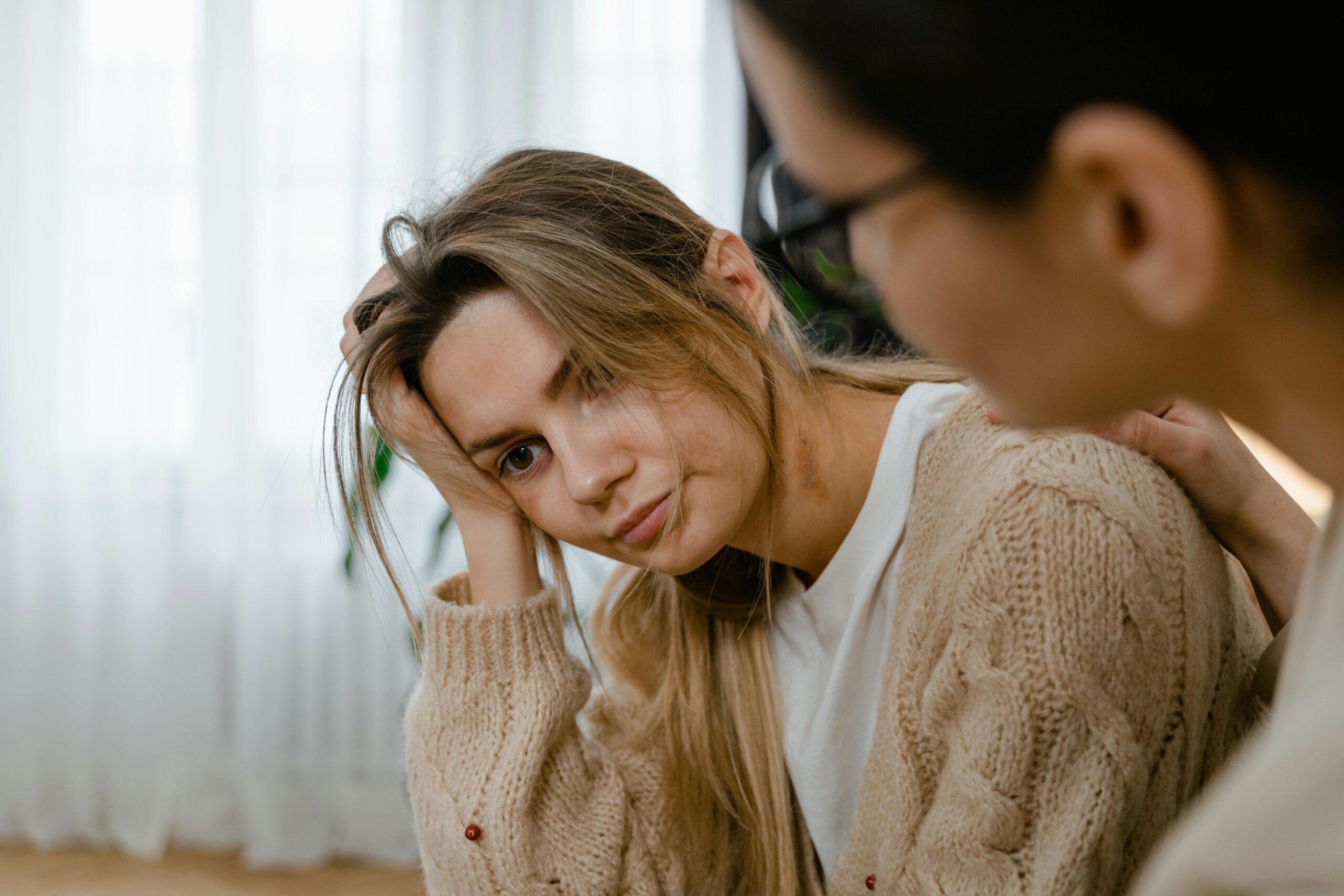 A woman resting her head on her hand, looking anxious as she is comforted by a friend, symbolizing the challenge of practicing patience while manifesting your dream life."