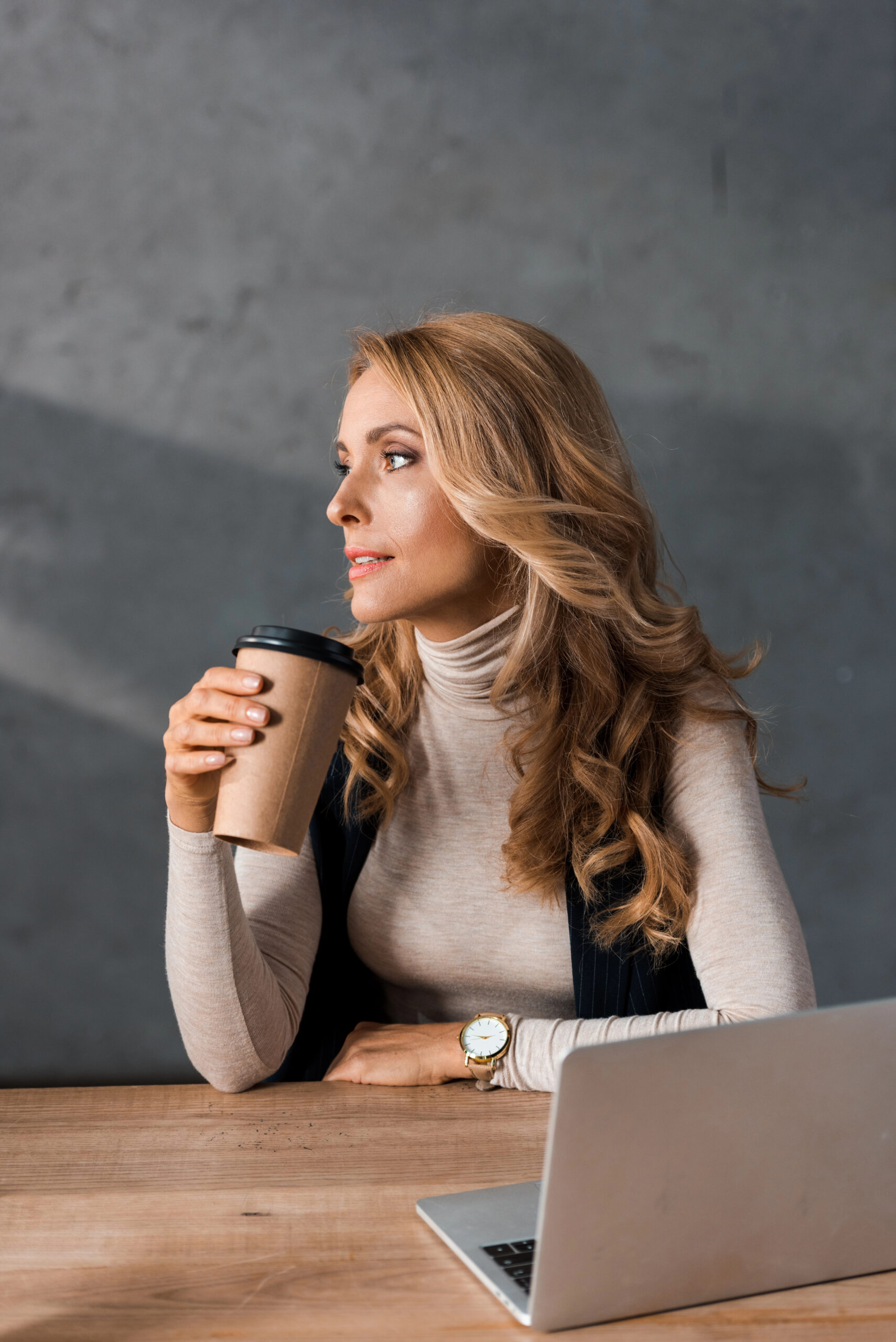 Woman sitting at her desk, holding a cup of coffee, deep in thought about life-changing habits for personal growth and success.