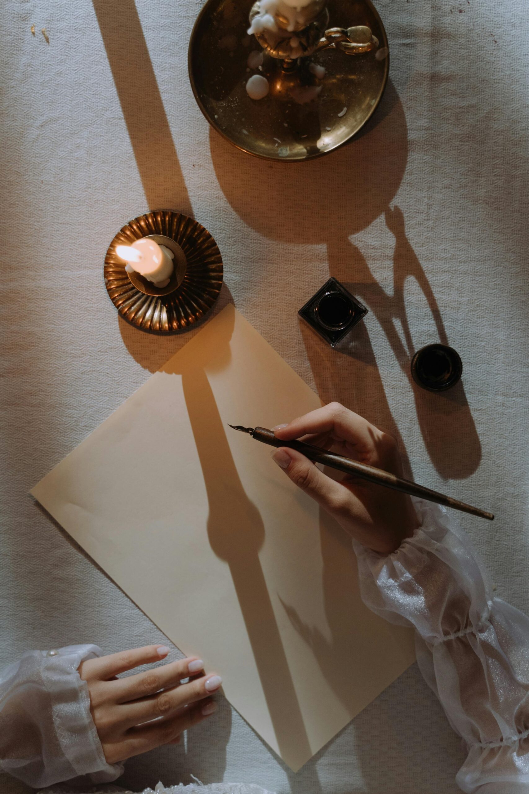 A desk with a lit candle, crystals, and a blank page where a woman’s hand is holding a pen, creating a serene and focused atmosphere.