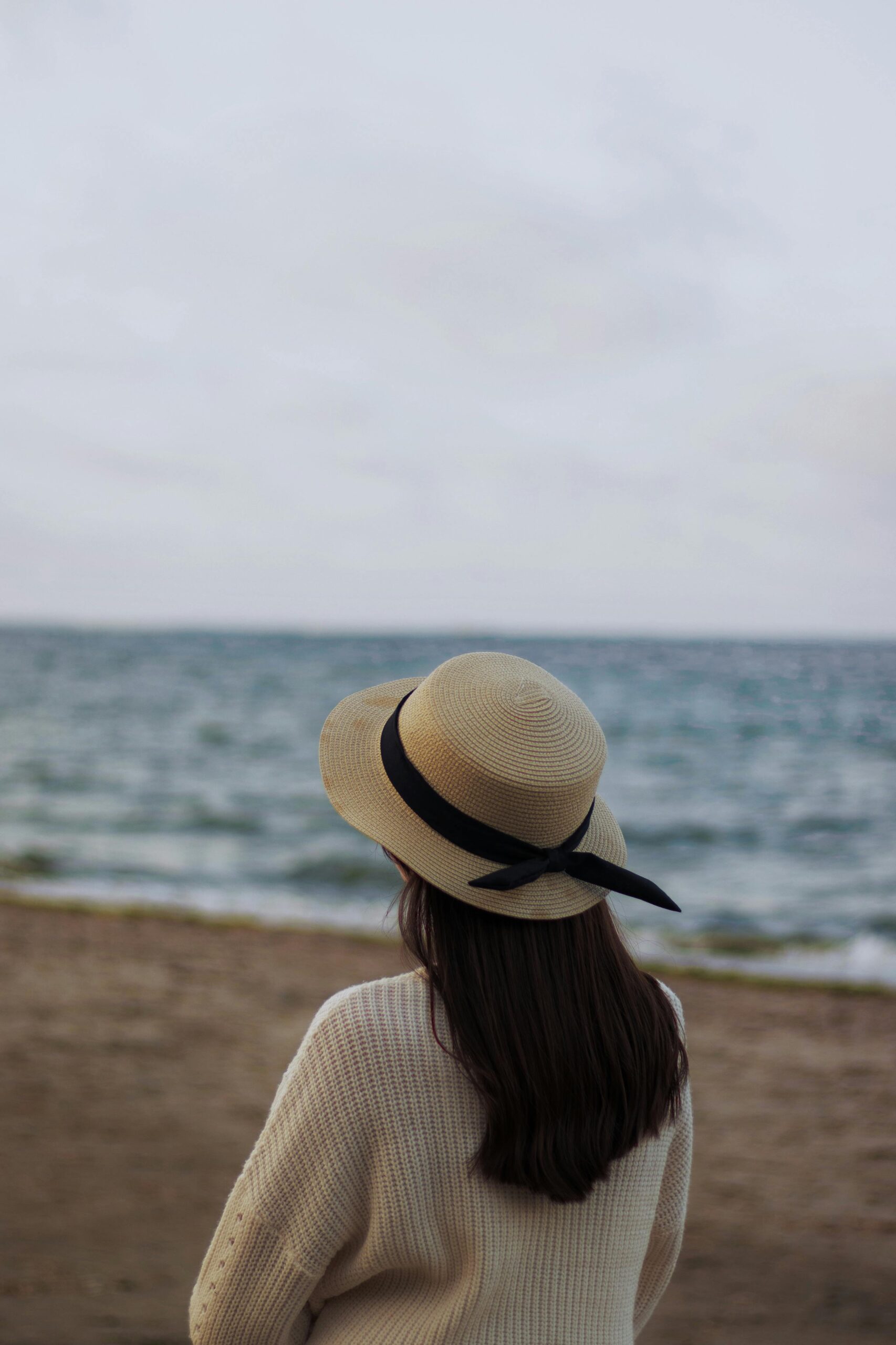 Woman gazing at the ocean on a cool, cloudy day, embracing slow living and mindfulness.