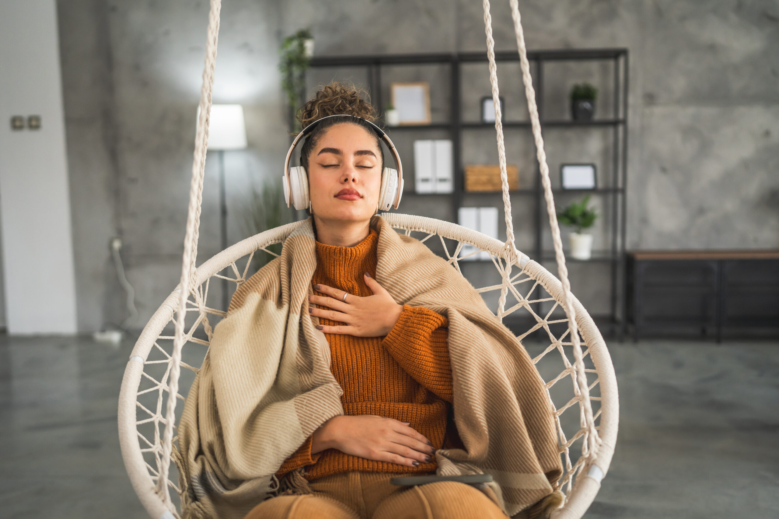 A woman sitting on a swing, eyes closed, with her hand on her heart, meditating in a peaceful, serene environment.