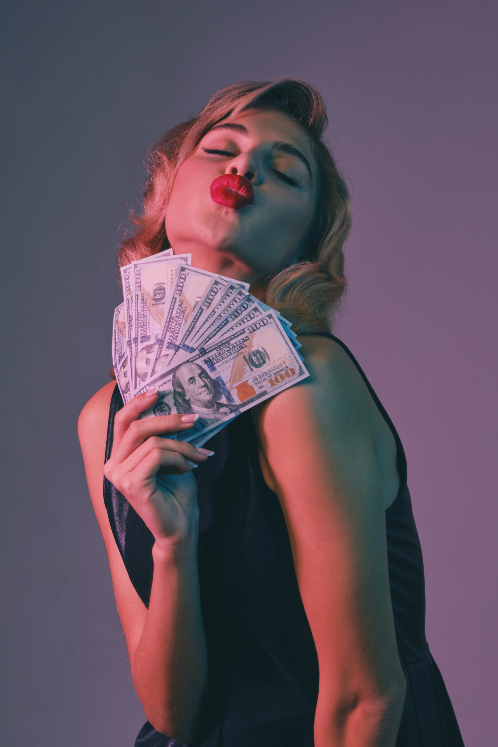 Confident woman holding a fanned-out stack of money, making a kiss face, celebrating financial abundance and wealth attraction.