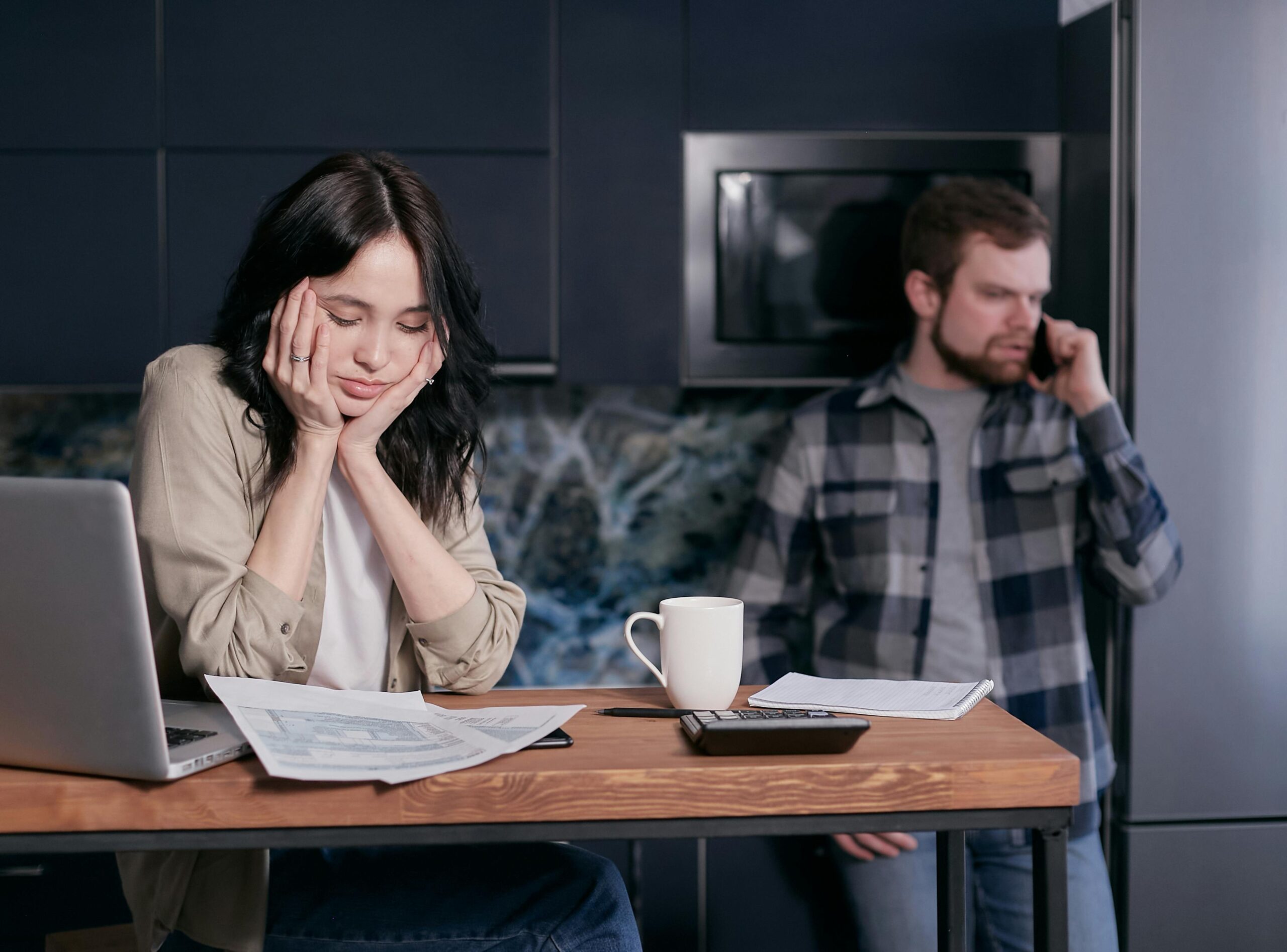 A stressed couple sitting in their kitchen, overwhelmed by bills and learning how to overcome money blocks.