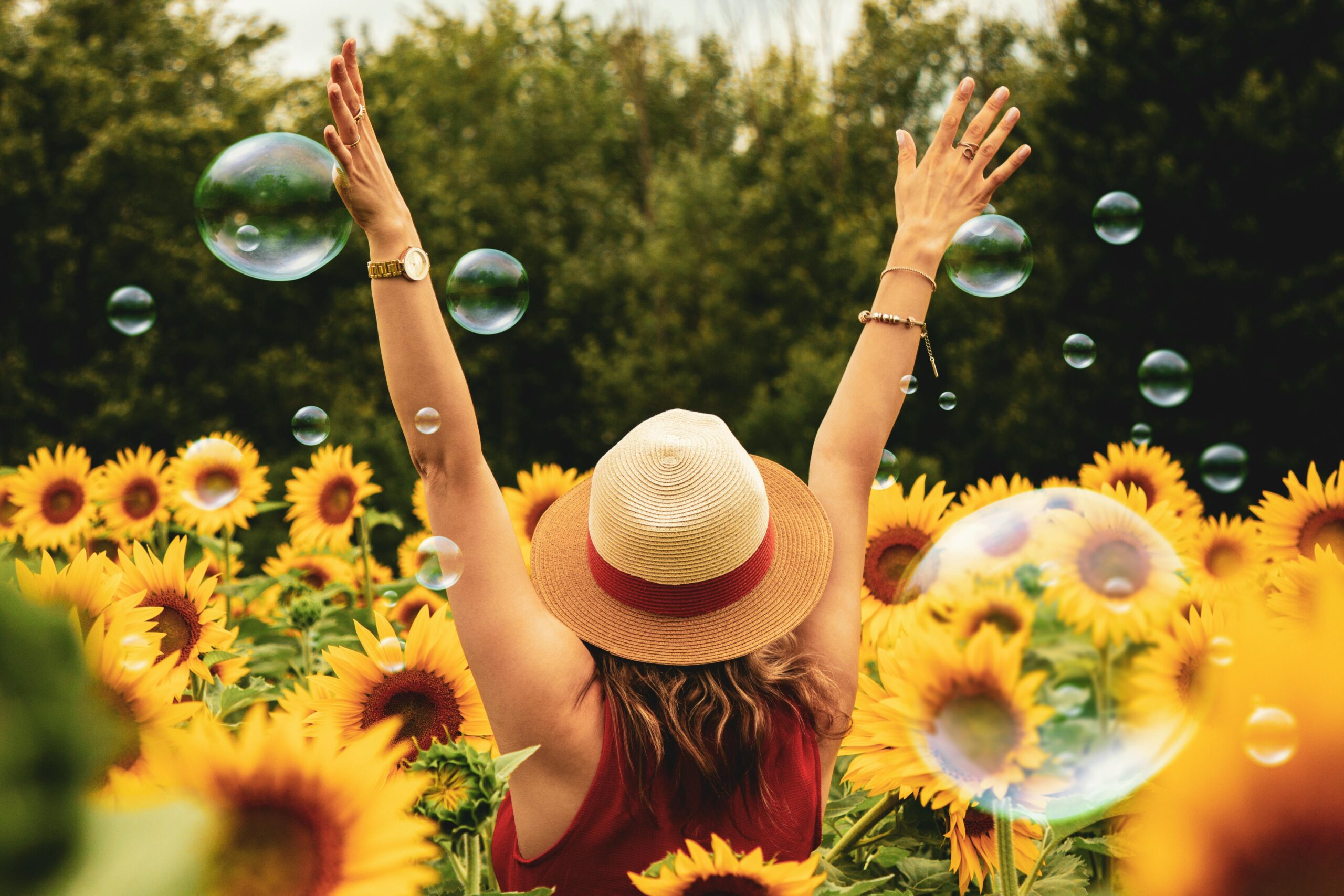 Woman with arms outstretched in a sunflower field, surrounded by bubbles, embracing joy and slow living.