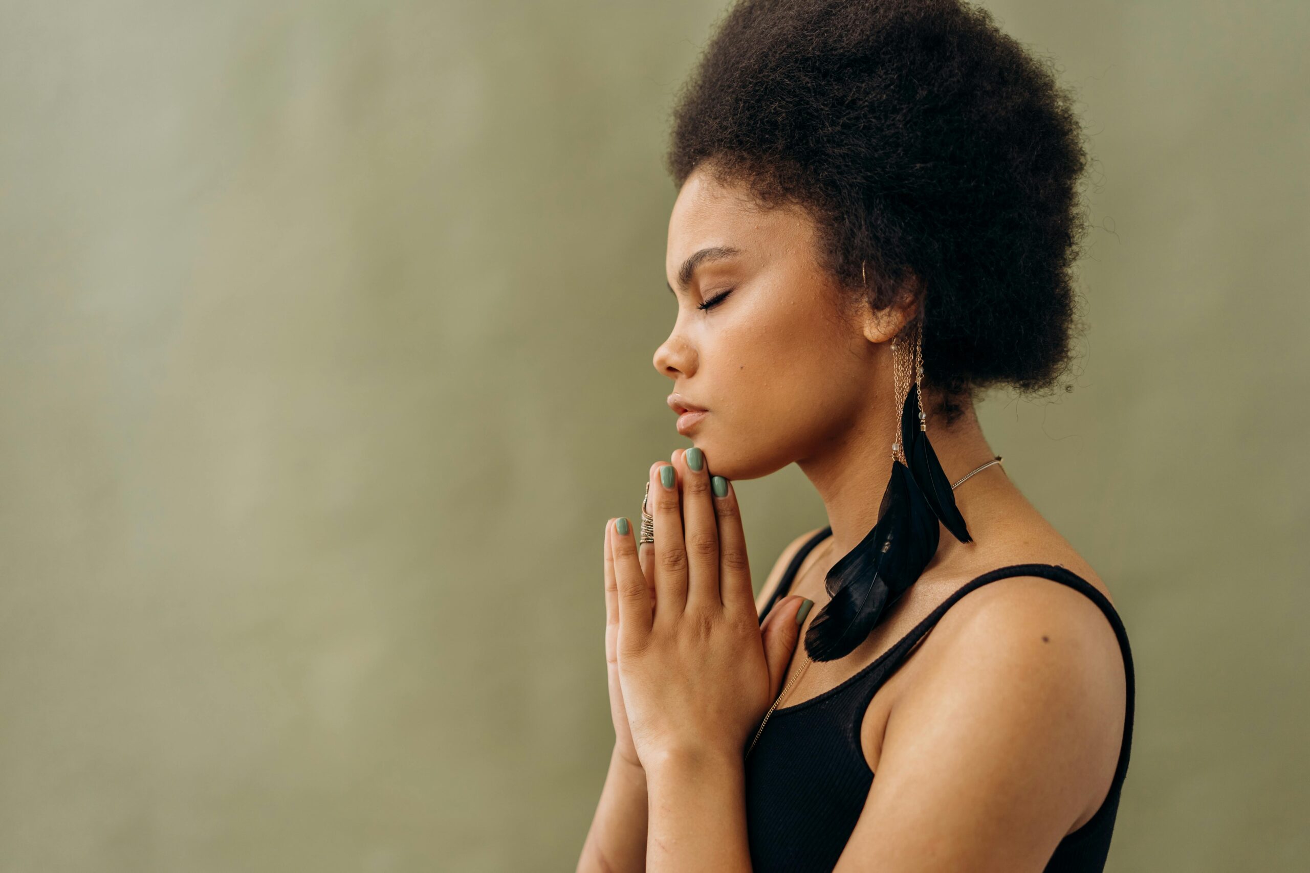 Side profile of a beautiful woman with her eyes closed, using the best beginner manifestation techniques with her hands in a prayer position to her chin.