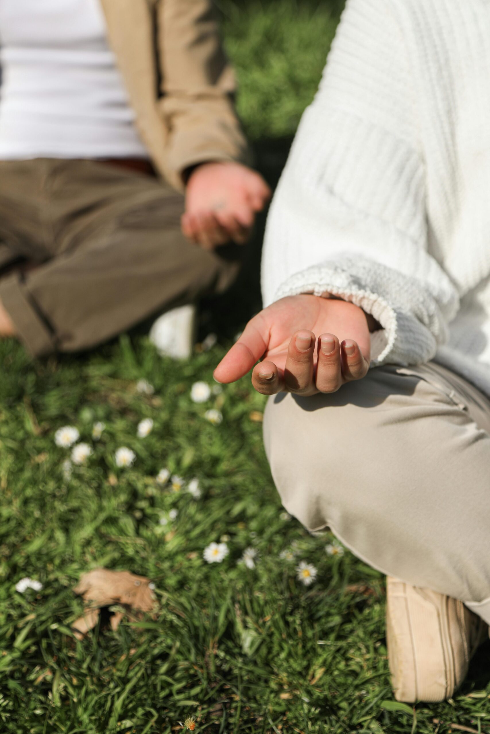 Two people sitting close together in the grass, with hands resting on knees in a meditative position, focusing on breathwork for manifestation.