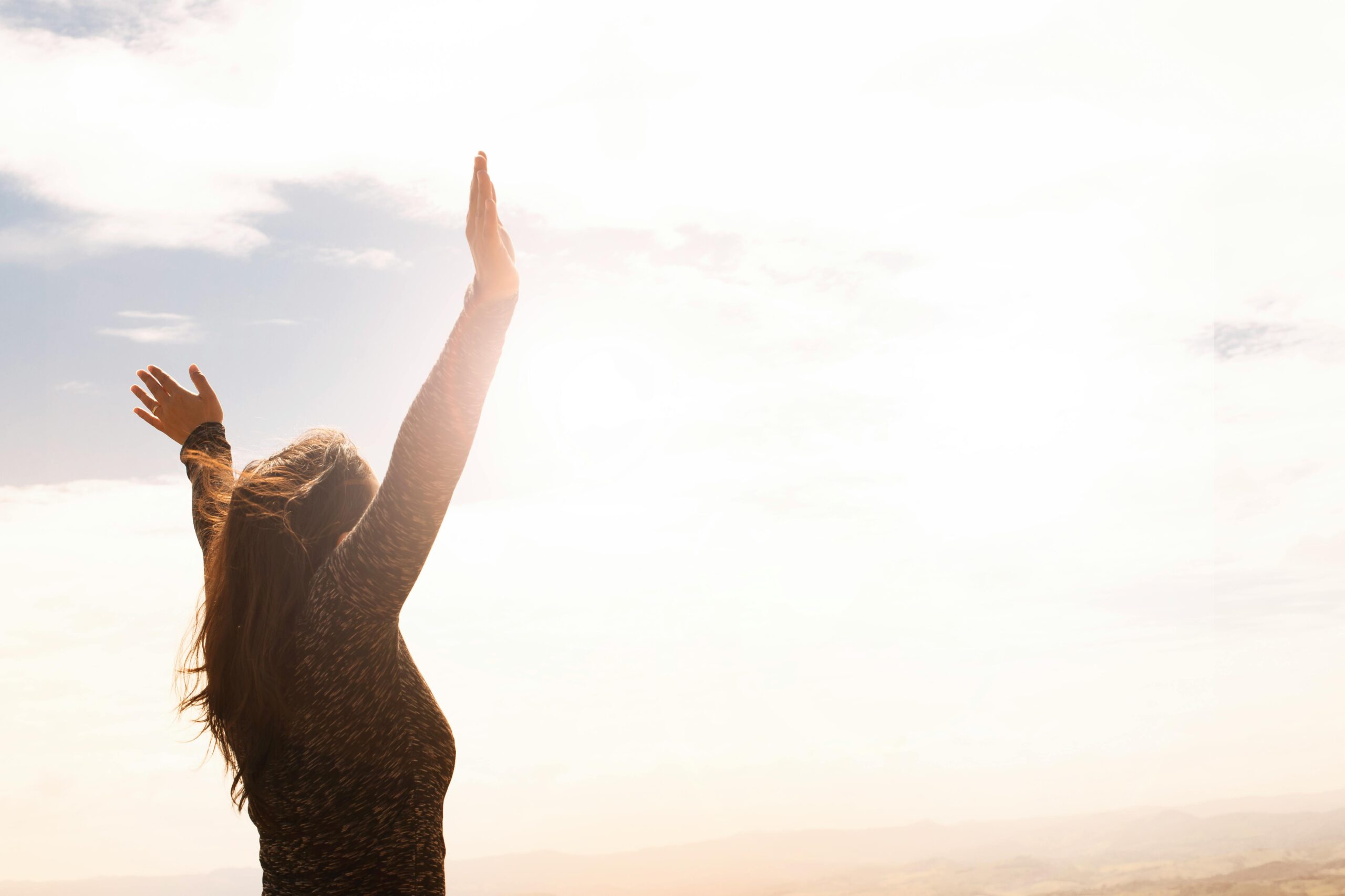 A woman standing in nature with arms open, symbolizing conscious living and living intentionally.