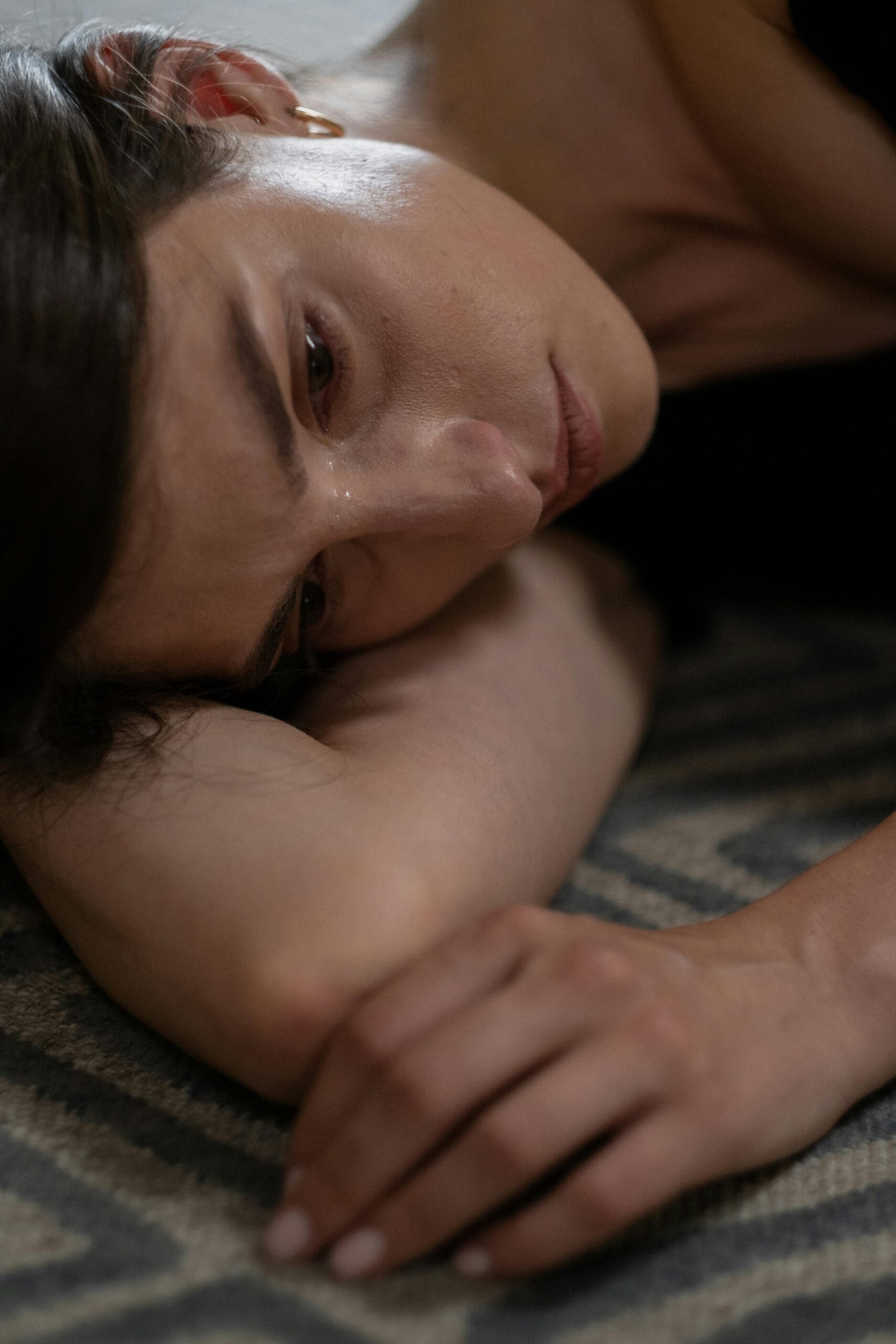 Close-up of a woman lying on the ground, dissociating with tears streaming down her face, depicting emotional distress and nervous system dysregulation.