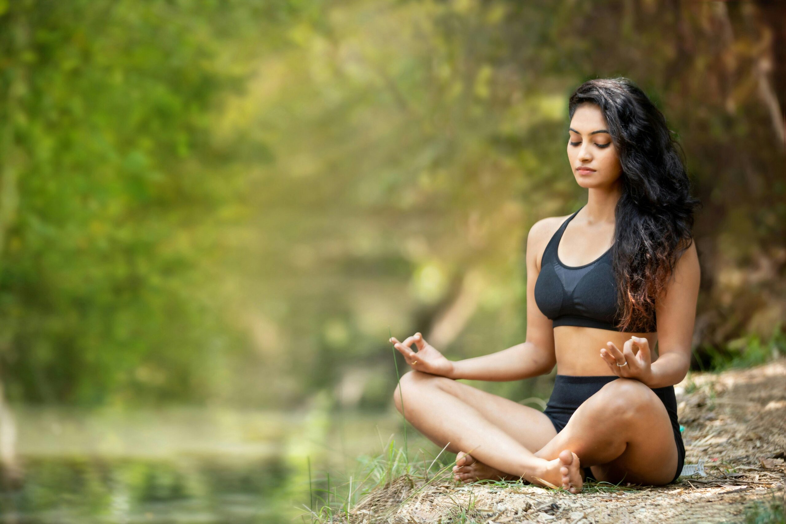 Woman meditating outdoors in nature, sitting cross-legged, symbolizing calmness and balance during a nervous system detox.