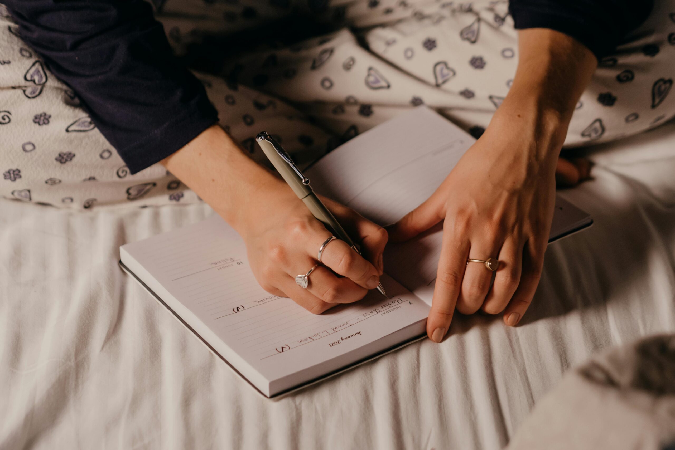 A woman journaling in bed as part of her slow evenings routine, surrounded by soft lighting and cozy blankets, creating a peaceful and intentional night ritual.