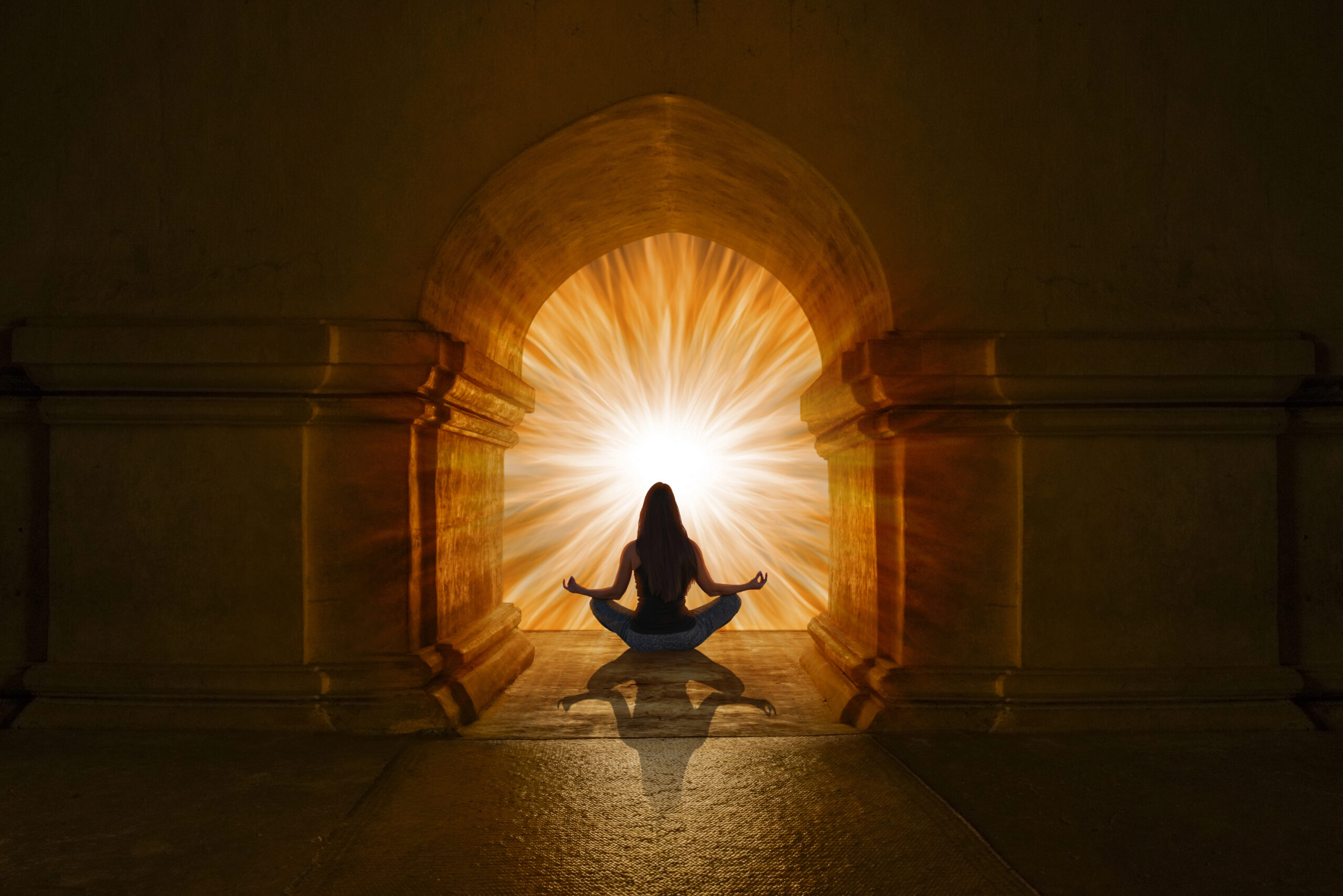A woman meditating in front of a glowing portal of light, symbolizing spiritual awakening and higher consciousness, often associated with crystals for head chakra healing.