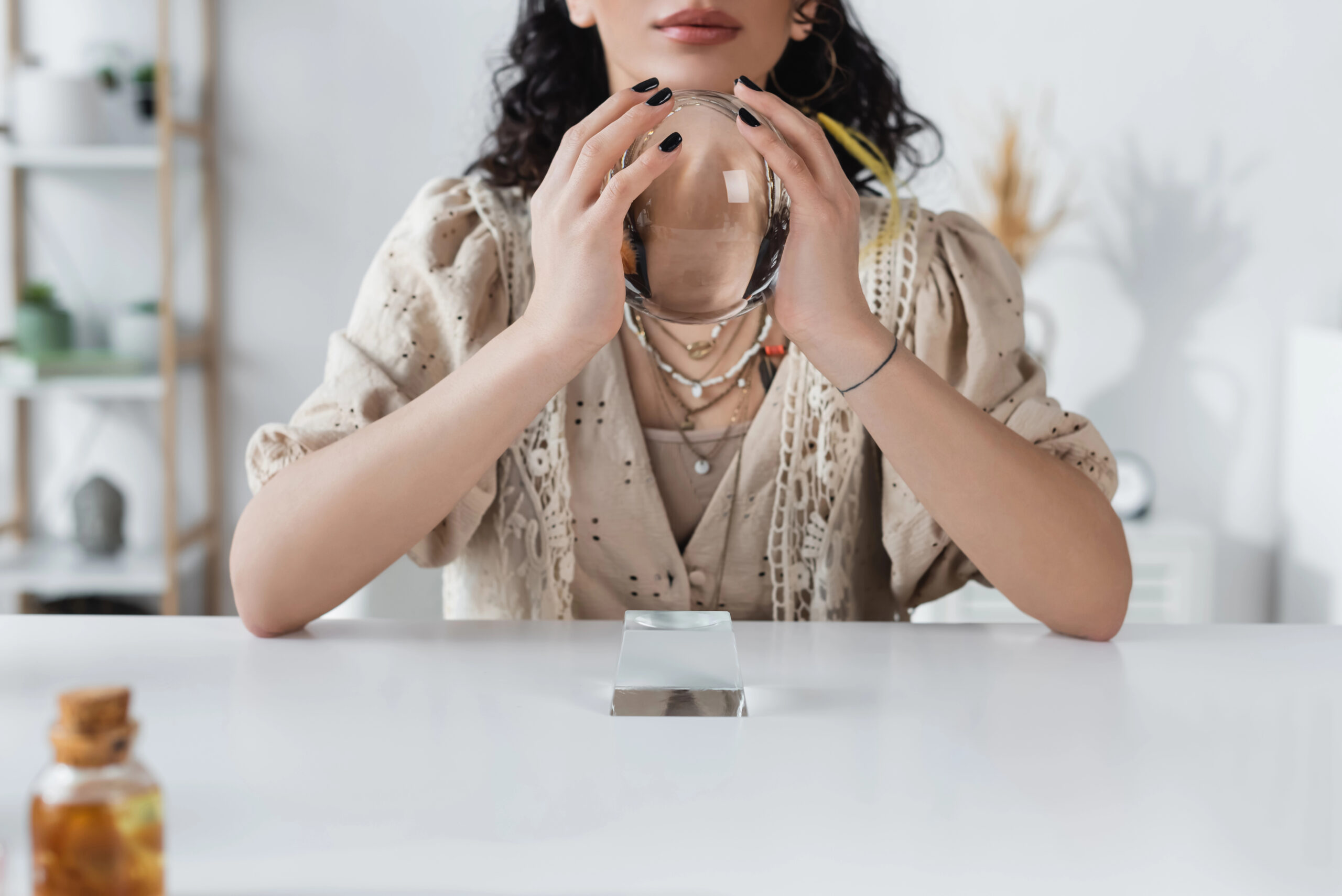 A woman holding a clear crystal sphere on a white table, symbolizing crystals for knowledge, mental clarity, and intuitive learning.